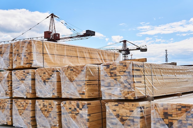 Empaquetado de tablas recién hechas y grúas en el fondo en el patio de la producción de carpintería