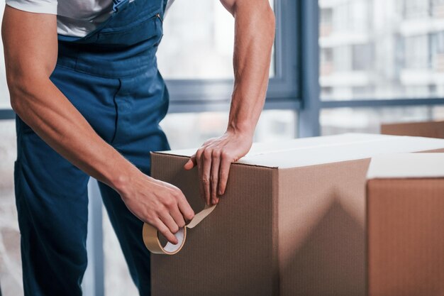 Empaquetando la caja El motor masculino joven en uniforme azul trabaja en el interior de la habitación