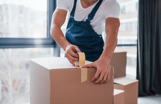 Empaquetando la caja El motor masculino joven en uniforme azul trabaja en el interior de la habitación