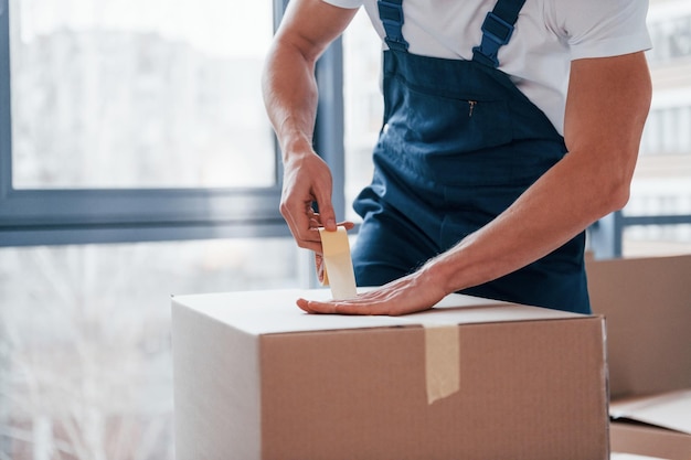 Empaquetando la caja El motor masculino joven en uniforme azul trabaja en el interior de la habitación