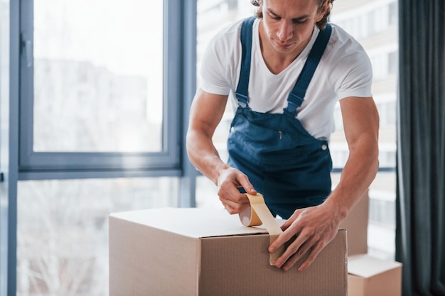 Empaquetando la caja El motor masculino joven en uniforme azul trabaja en el interior de la habitación