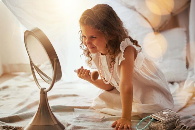 Empiezan tan jóvenes Foto de una niña adorable aplicándose colorete en la cara en el espejo