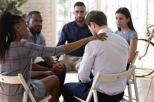 Foto empleada afroamericana compasiva poniendo la mano en el hombro de compañeros de trabajo desesperados apoyando expresar condolencias equipo diverso de raza mixta de trabajadores sentados en círculo en terapia de grupo