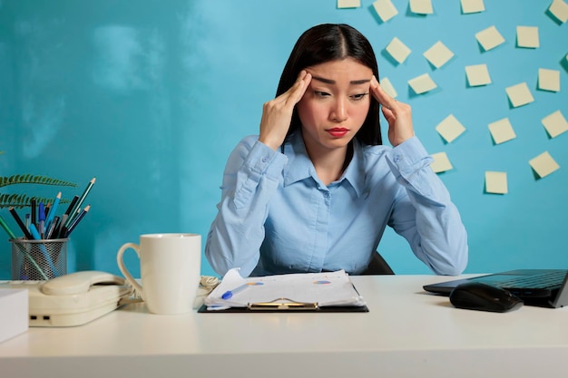 Empleada corporativa con exceso de trabajo frotando las sienes tratando de hacer el papeleo antes del final del día. Mujer estresada sentada frente a una laptop tratando de ordenar ideas en su mente.