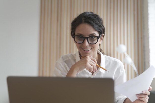 Empleada feliz mirando la pantalla del portátil con una sonrisa leyendo el correo electrónico con buenas noticias en el trabajo