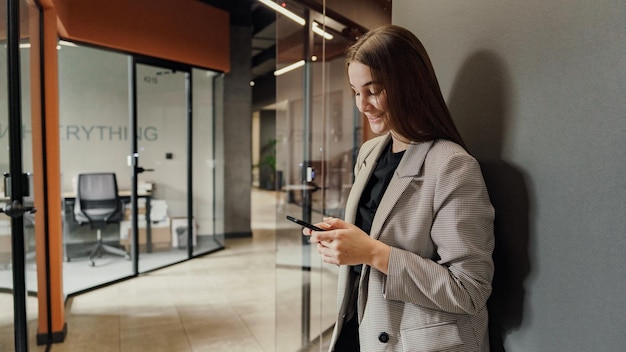 Una empleada de oficina una mujer de negocios con ropa de negocios usa un teléfono y una aplicación de negocios