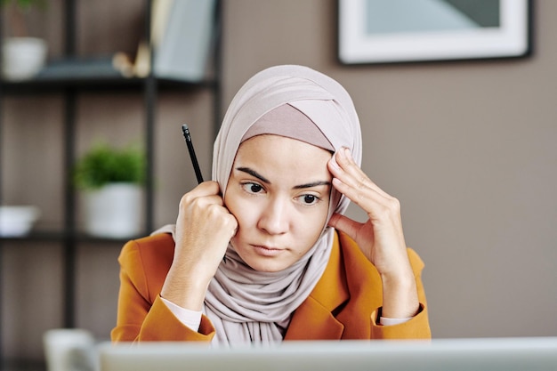 Empleada seria en hijab mirando atentamente la pantalla del portátil