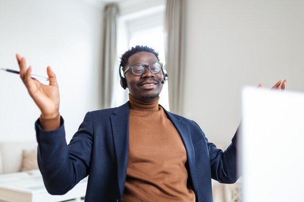 Foto empleado afroamericano sonriente con auriculares usando una computadora portátil mirando la pantalla haciendo una llamada de video o viendo un seminario web escribiendo notas aprendizaje a distancia concepto de lenguaje operador de centro de llamadas trabajando