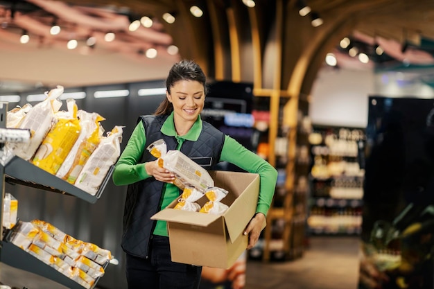 Foto un empleado de almacén está mostrando pan en los estantes mientras está de pie en el supermercado