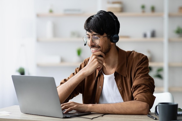 Empleado árabe alegre viendo videos mientras toma un descanso para tomar café