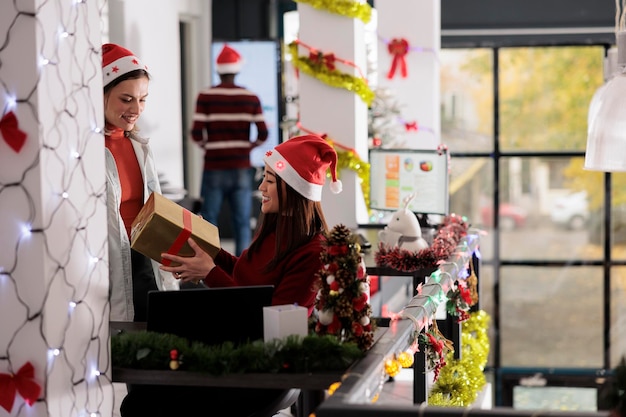 Foto un empleado asiático feliz y sonriente sorprendido con un regalo secreto de santa claus de un compañero de trabajo en una oficina decorada festivamente un trabajador alegre y alegre recibe un regalo de navidad durante la temporada de vacaciones de invierno