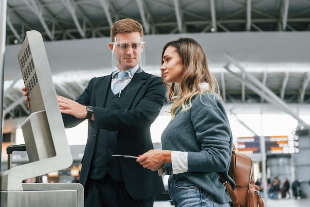 Empleado ayudando a usar la terminal Joven turista está en el aeropuerto durante el día