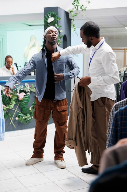 Empleado del centro comercial ayudando a un comprador afroamericano a elegir una camisa. Asistente de boutique de moda que ayuda al cliente a comprar ropa informal moderna y examina el tamaño adecuado