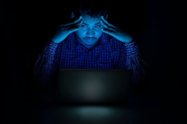 Empleado corporativo que se siente cansado y con dolor de cabeza mientras trabaja hasta tarde en la noche en la computadora portátil