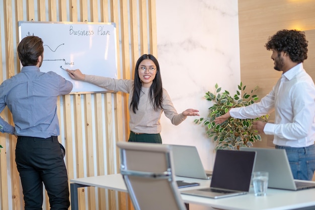 Empleado de la empresa señalando con un marcador la línea horizontal del gráfico dibujado en la pizarra a sus colegas