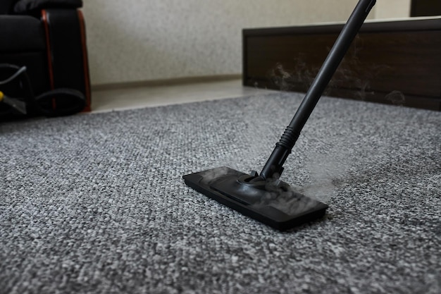 Empleado de la empresa de servicios de limpieza quitando la suciedad de la alfombra en un piso con equipo profesional de limpieza a vapor de cerca