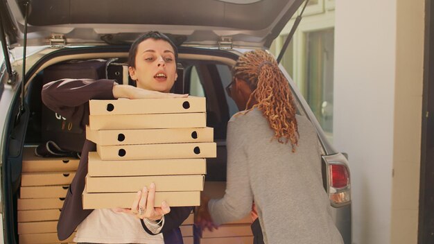 Empleado de entrega de alimentos entregando un gran pedido de cajas de pizza al cliente, entregando paquetes de comida del maletero del vehículo a las personas. mensajero de pizzería tomando pilas de comida rápida para el cliente del servicio de entrega.