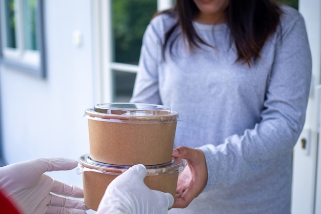 Un empleado con guantes está enviando cajas de comida a los clientes en la puerta, de acuerdo con el pedido. Concepto de entrega, entrega en línea