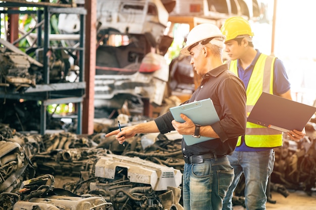 Empleado ingeniero que trabaja con el gerente, comprobando el inventario de existencias en el garaje, tienda de piezas de automóvil de motor usado