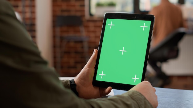 Empleado de inicio mirando una tableta digital con pantalla verde, usando un dispositivo con un espacio de copia de maqueta aislado y una plantilla de clave de croma en blanco. Fondo y pantalla del dispositivo. De cerca.