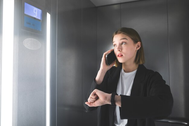 Empleado joven está mirando el número de piso en el ascensor hablando por teléfono inteligente.