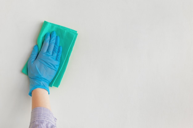 Empleado de la mano en un guante protector de goma azul que limpia la pared del polvo con un trapo seco.