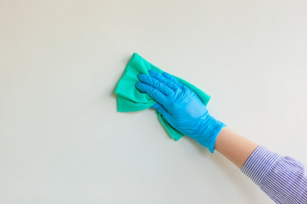 Empleado de la mano en un guante protector de goma azul que limpia la pared del polvo con un trapo seco.