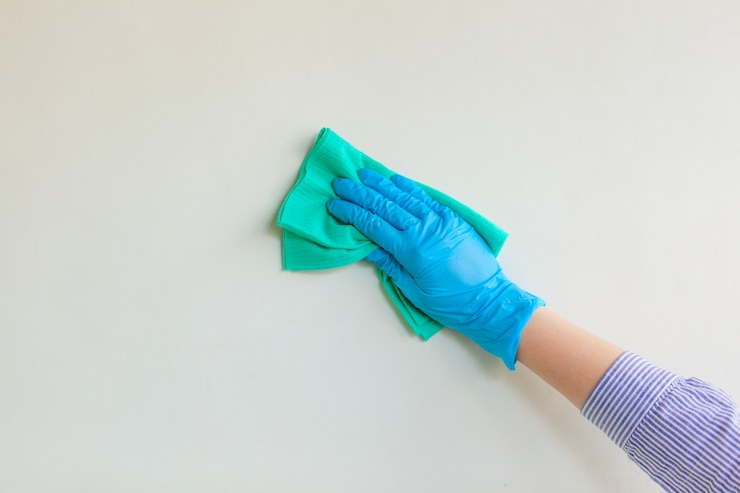 Foto empleado de la mano en un guante protector de goma azul que limpia la pared del polvo con un trapo seco.