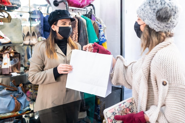 Empleado con máscaras en una tienda de ropa entregando ropa a un cliente, medidas de seguridad en la pandemia de coronavirus, covid-19