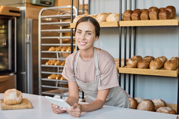 Empleado de panadería contemporáneo con tableta mientras se desplaza por el nuevo surtido