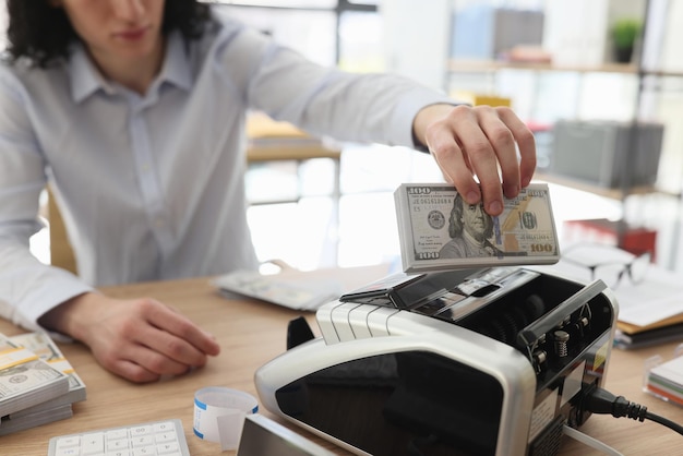 Foto el empleado de pelo largo pone una pila de dinero en el contador de billetes. el hombre se sienta en la mesa contando.