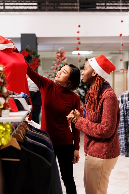 Foto empleado presentando ropa al cliente, mujer asiática buscando artículos de moda para regalar como regalos de navidad en la tienda minorista. al gerente de compras recomendando accesorios para los preparativos de la cena.