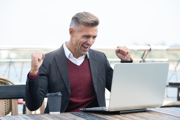 Un empleado profesional feliz hace un gesto ganador trabajando en una laptop afuera, gana