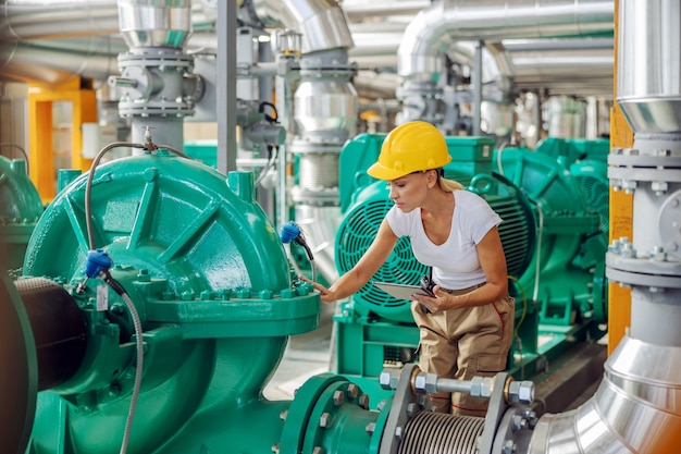 Empleado sosteniendo la tableta y controlando el calor en la turbina mientras está de pie en la planta de calefacción