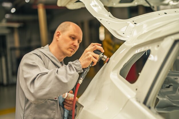 Empleado del taller de pintura de una planta de automóviles Lijado de la pieza pintada con herramienta neumática