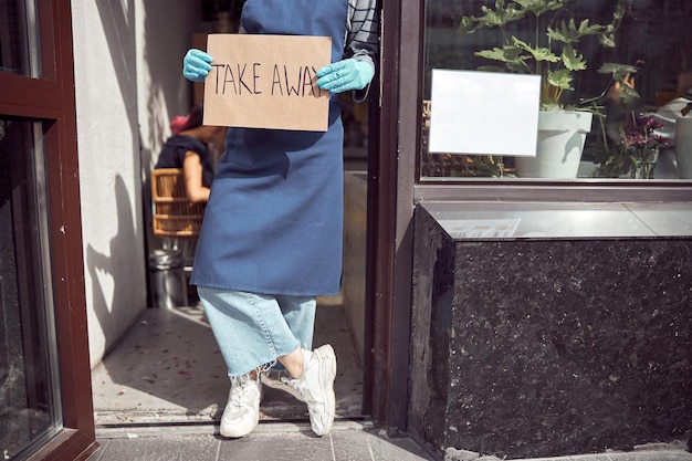 Empleador asiático sosteniendo cartel para llevar antes de la entrada del café