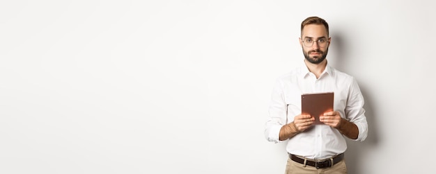 Empleador serio que trabaja con lectura de tabletas digitales en gafas de pie sobre fondo blanco