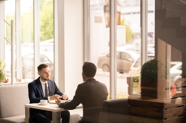 El empleador y el solicitante en ropa formal tienen una conversación sobre los términos de empleo mientras están sentados uno frente al otro en la mesa del café