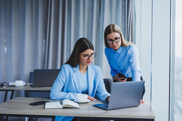 Empleados alegres charlando mientras trabajan en una laptop discutiendo el trabajo durante un descanso para tomar café en la oficina una mujer de negocios con anteojos escucha a un colega tiene una agradable conversación amistades