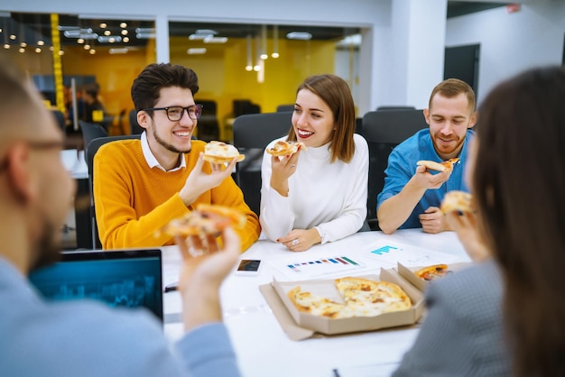 Empleados alegres y diversos comiendo pizza juntos durante el descanso en la oficina Concepto de negocio
