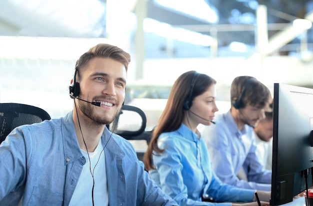 Empleados del centro de llamadas sonrientes sentados en línea con sus auriculares.