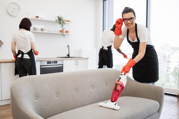 Empleados felices de la compañía de limpieza limpiando en la cocina luminosa y espaciosa de la casa