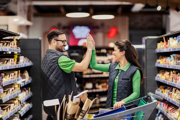 Los empleados felices del supermercado organizan con éxito las compras en el pasillo y chocan los cinco
