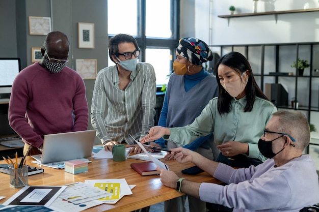 Empleados interculturales contemporáneos con máscaras discutiendo datos en una reunión