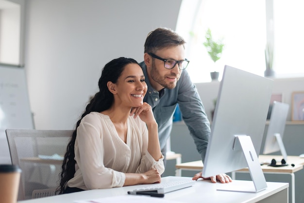 Empleados masculinos y femeninos sonrientes discutiendo un proyecto de negocios usando una computadora en la copia de la oficina de la empresa