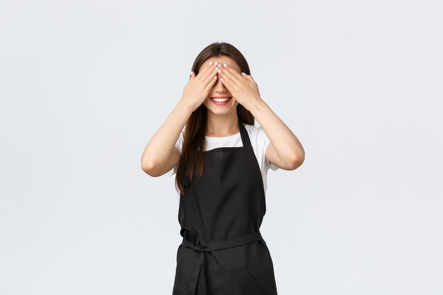 Empleados de la tienda de abarrotes, concepto de pequeñas empresas y cafeterías. Emocionado y feliz linda mujer barista cerró los ojos como anticipando sorpresa, esperando regalo, de pie fondo blanco.