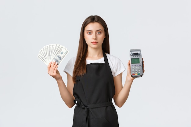 Empleados de la tienda de abarrotes, concepto de pequeñas empresas y cafeterías. Vendedora o barista en delantal negro con efectivo y terminal de pago POS, mostrando dos formas de comprar artículos en la tienda.