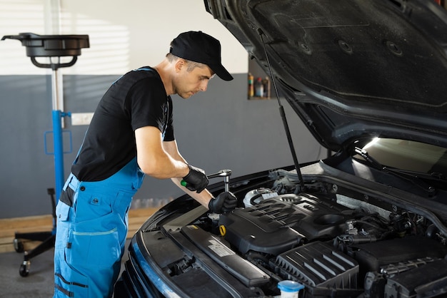 Empoderar a un mecánico masculino está trabajando en el servicio de automóviles. El hombre está trabajando en un mantenimiento habitual de automóviles.