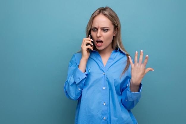 Foto empörte süße blonde frau, die am telefon auf einem blauen hellen hintergrund plaudert