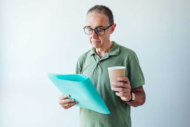 Empreendedor aposentado, vestindo uma camisa verde e óculos, segurando uma pasta com um relatório e um café